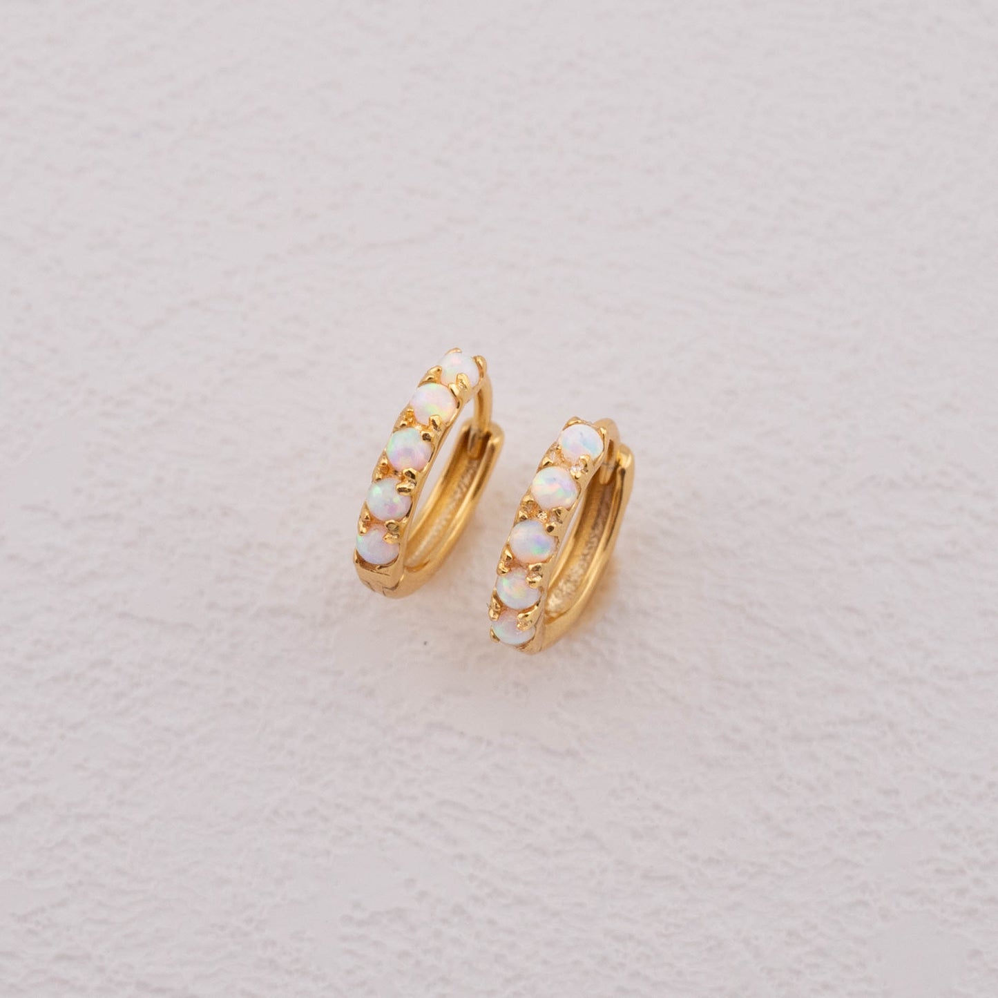 Opal hoop earrings with a detailed close-up of white opal stones set in gold.
