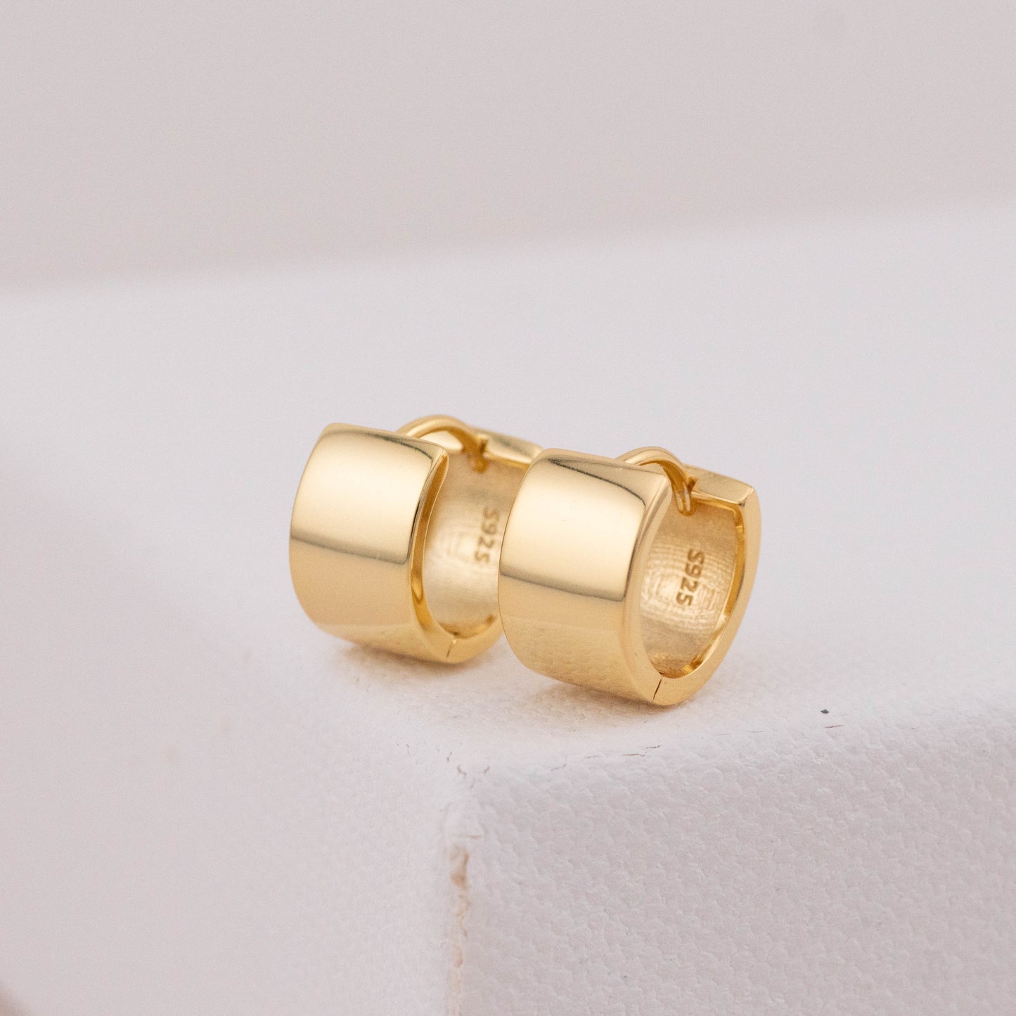 Chunky hoop earrings in gold with a close-up of the S925 stamp on the inner side.