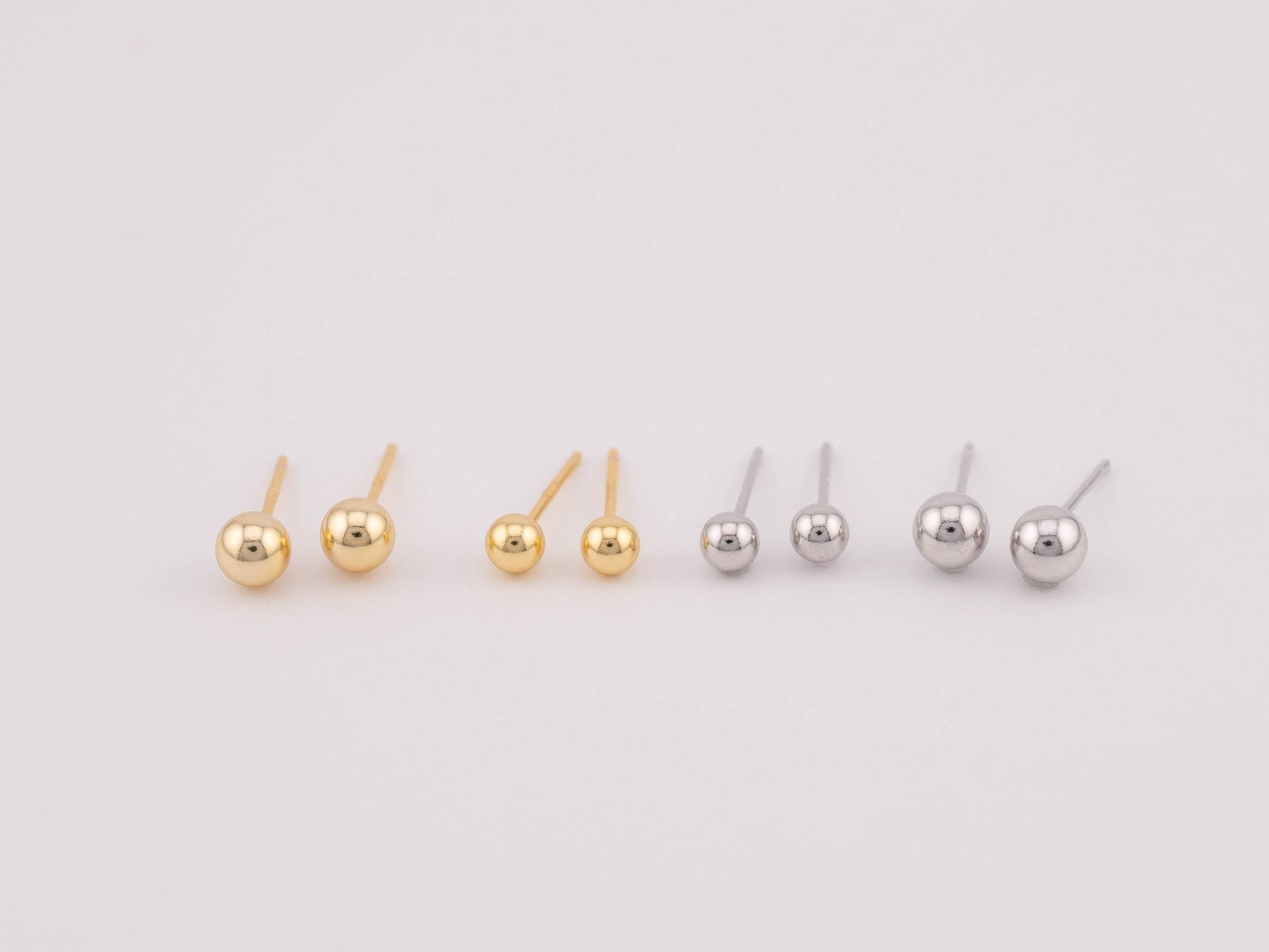 Front view photo featuring four sets of gold and silver ball earrings with two different sizes each, arranged side by side for size comparison. Suitable for sale as a set, offering versatility in size options and a stylish addition to any jewelry collection.