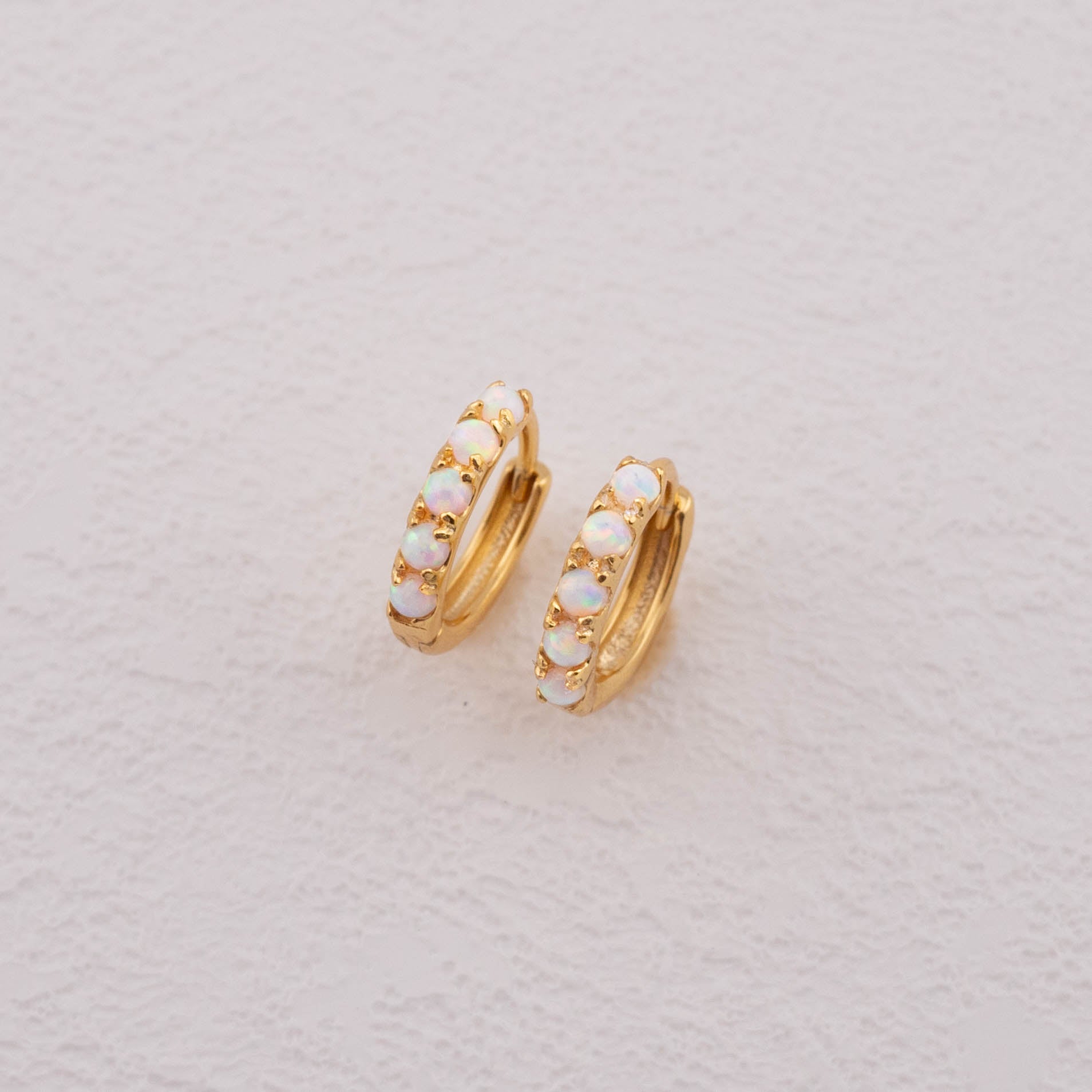 Opal hoop earrings with a detailed close-up of white opal stones set in gold.